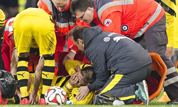 Borussia Dortmund's Marco Reus covers his face in agony as he receives treatment on the field.